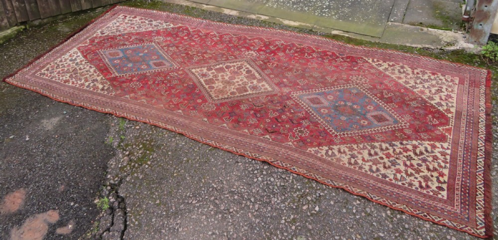 An antique hand-knotted Khamseh tribal kelleh carpet with a dark red field, geometric diamond medallions, and small bird motifs.