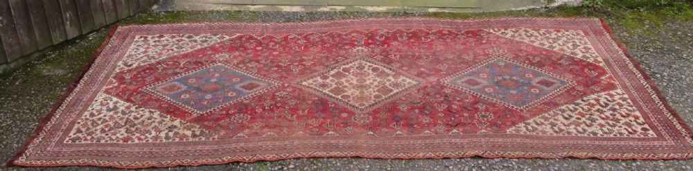 An antique hand-knotted Khamseh tribal kelleh carpet with a dark red field, geometric diamond medallions, and small bird motifs. View II