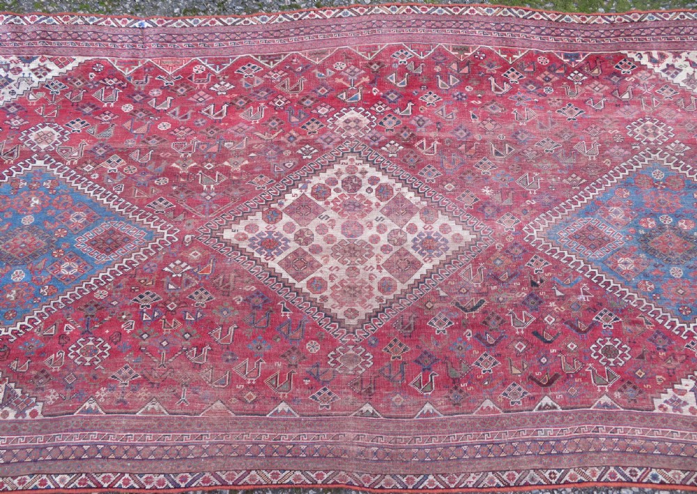 An antique hand-knotted Khamseh tribal kelleh carpet with a dark red field, geometric diamond medallions, and small bird motifs. View V