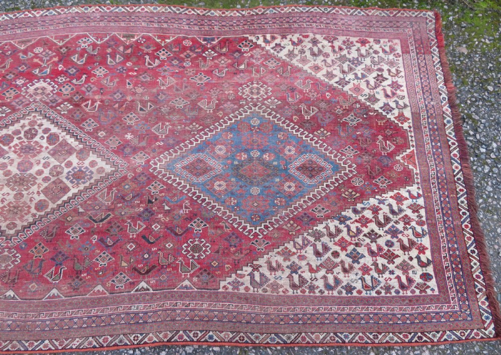 An antique hand-knotted Khamseh tribal kelleh carpet with a dark red field, geometric diamond medallions, and small bird motifs. View VI