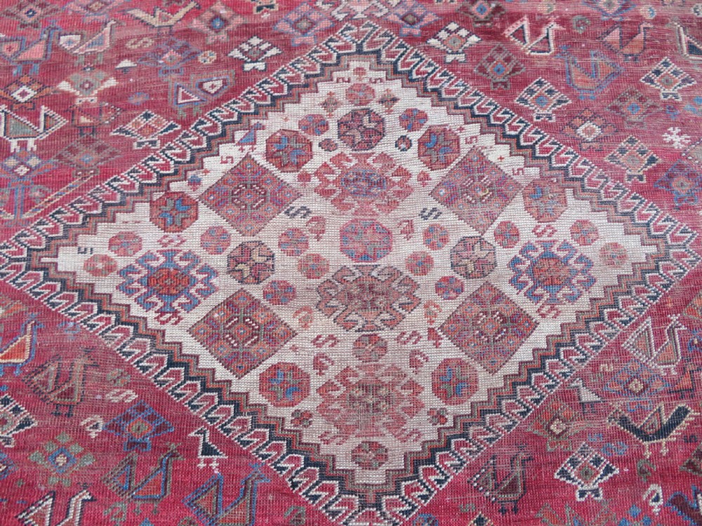 An antique hand-knotted Khamseh tribal kelleh carpet with a dark red field, geometric diamond medallions, and small bird motifs. View IX