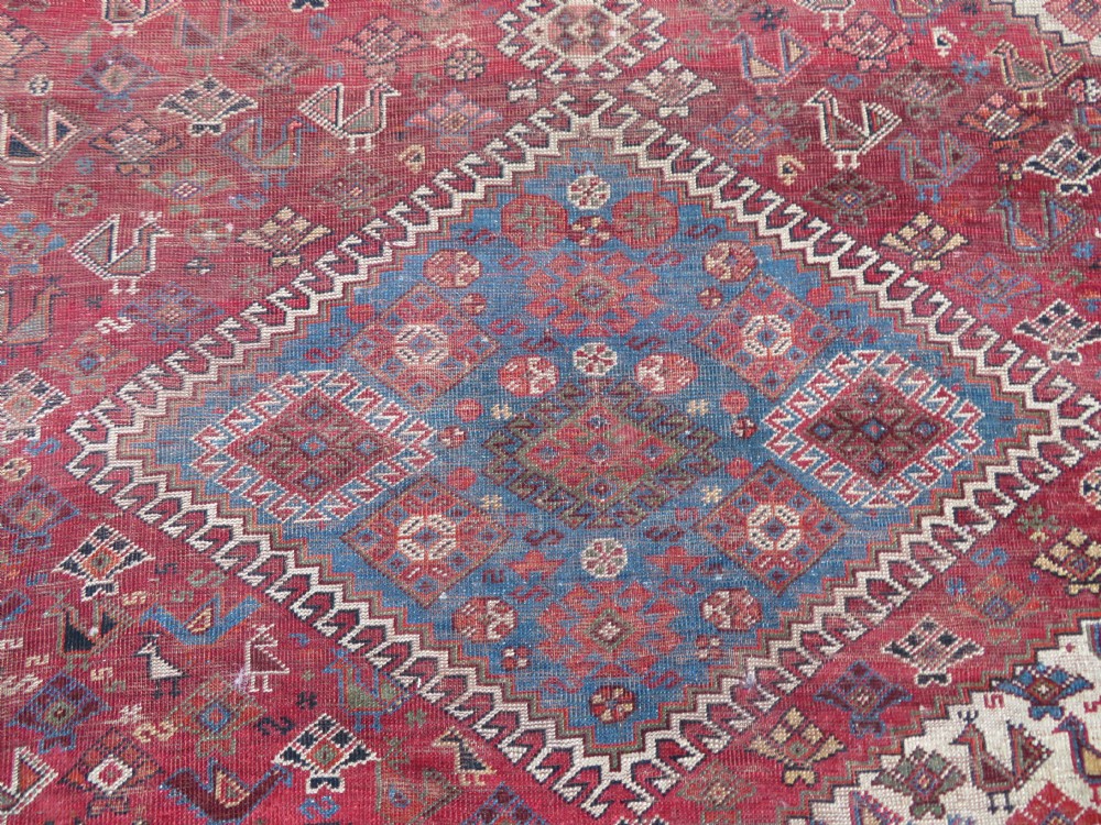 An antique hand-knotted Khamseh tribal kelleh carpet with a dark red field, geometric diamond medallions, and small bird motifs. View X