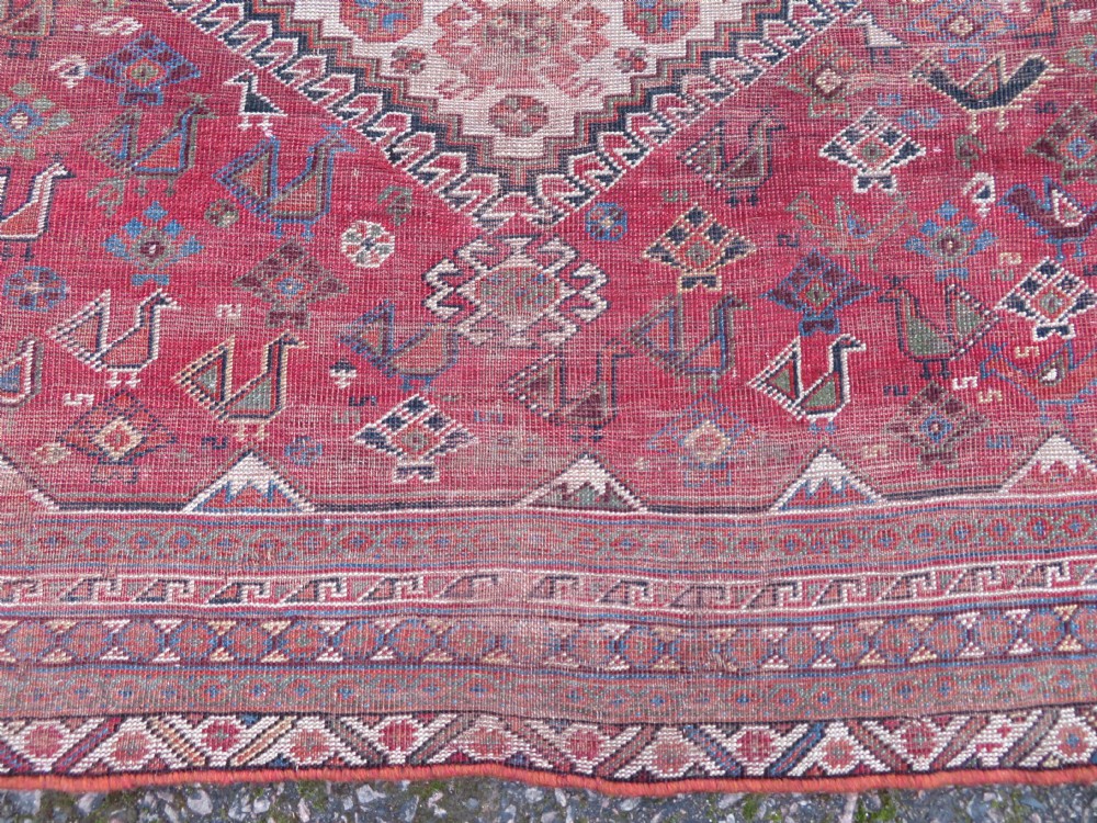 An antique hand-knotted Khamseh tribal kelleh carpet with a dark red field, geometric diamond medallions, and small bird motifs. View XII