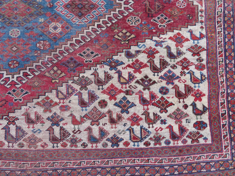 An antique hand-knotted Khamseh tribal kelleh carpet with a dark red field, geometric diamond medallions, and small bird motifs. View XIII