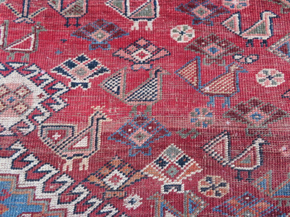 An antique hand-knotted Khamseh tribal kelleh carpet with a dark red field, geometric diamond medallions, and small bird motifs. View XV