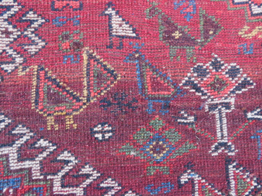 An antique hand-knotted Khamseh tribal kelleh carpet with a dark red field, geometric diamond medallions, and small bird motifs. View XXIV