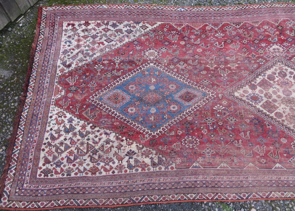An antique hand-knotted Khamseh tribal kelleh carpet with a dark red field, geometric diamond medallions, and small bird motifs. View IV