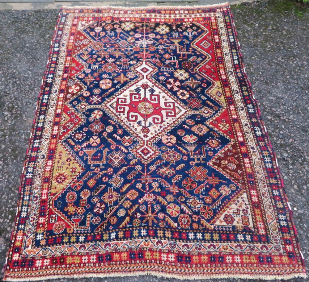 An antique hand-knotted Qashqai wool rug featuring a central ivory diamond medallion surrounded by detailed geometric and animal motifs on a navy blue field with a red border.