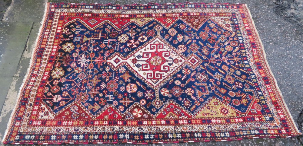 An antique hand-knotted Qashqai wool rug featuring a central ivory diamond medallion surrounded by detailed geometric and animal motifs on a navy blue field with a red border. View II