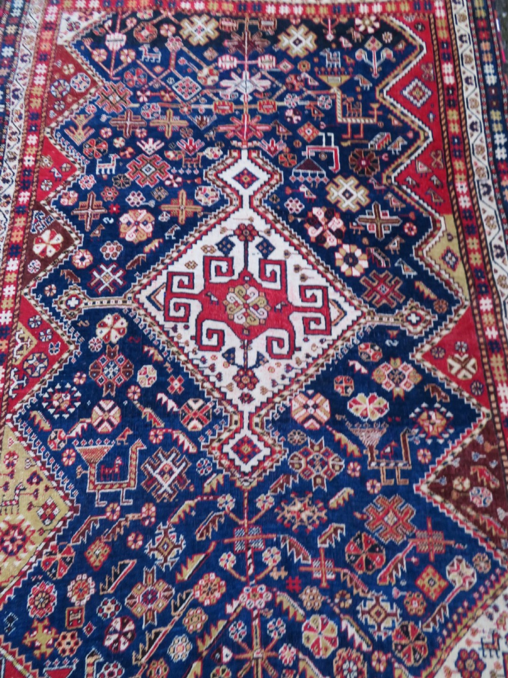 An antique hand-knotted Qashqai wool rug featuring a central ivory diamond medallion surrounded by detailed geometric and animal motifs on a navy blue field with a red border. View III