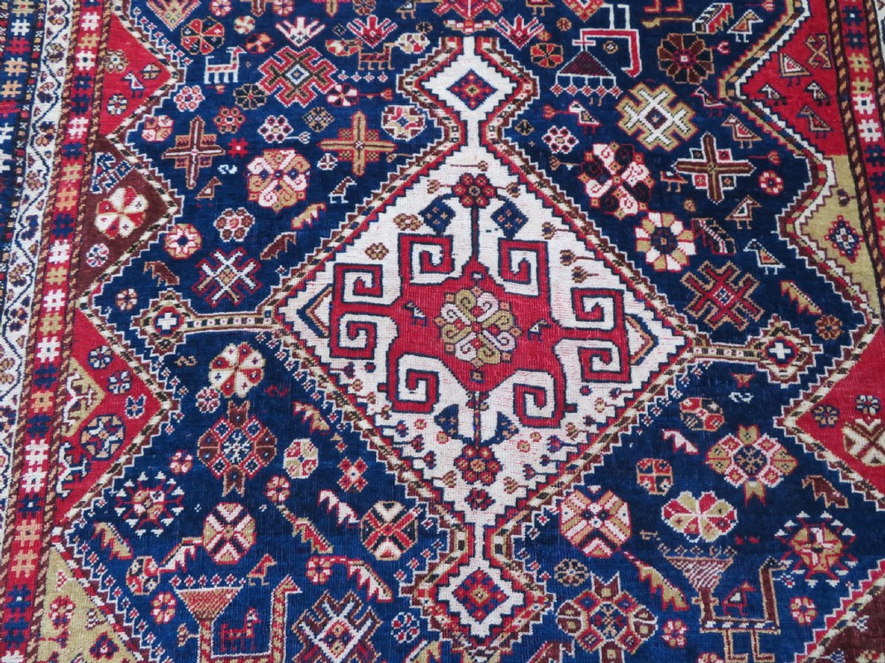 An antique hand-knotted Qashqai wool rug featuring a central ivory diamond medallion surrounded by detailed geometric and animal motifs on a navy blue field with a red border. View IV