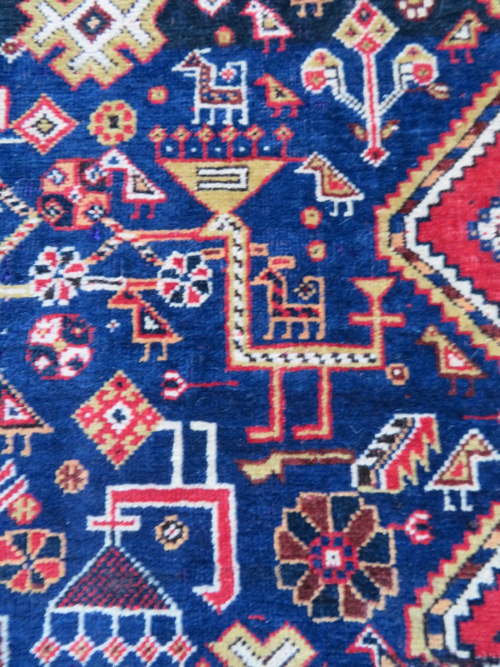 An antique hand-knotted Qashqai wool rug featuring a central ivory diamond medallion surrounded by detailed geometric and animal motifs on a navy blue field with a red border. View V