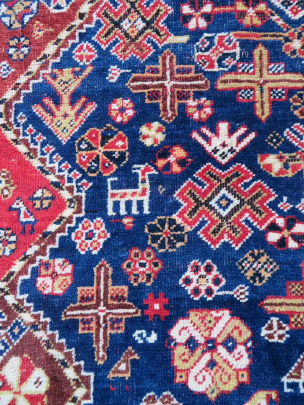 An antique hand-knotted Qashqai wool rug featuring a central ivory diamond medallion surrounded by detailed geometric and animal motifs on a navy blue field with a red border. View VI