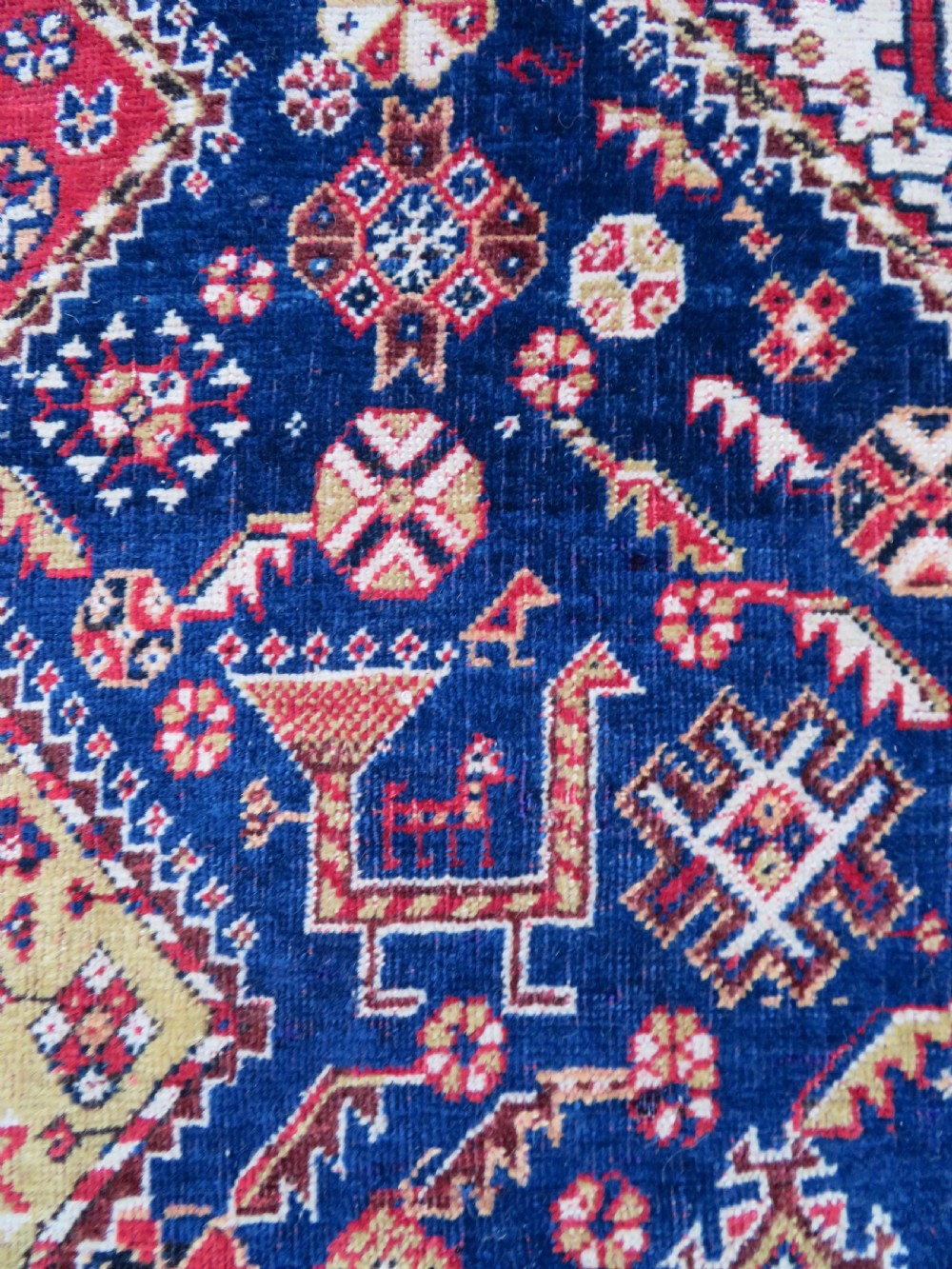 An antique hand-knotted Qashqai wool rug featuring a central ivory diamond medallion surrounded by detailed geometric and animal motifs on a navy blue field with a red border. View VII