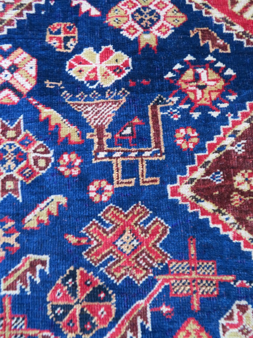 An antique hand-knotted Qashqai wool rug featuring a central ivory diamond medallion surrounded by detailed geometric and animal motifs on a navy blue field with a red border. View VIII