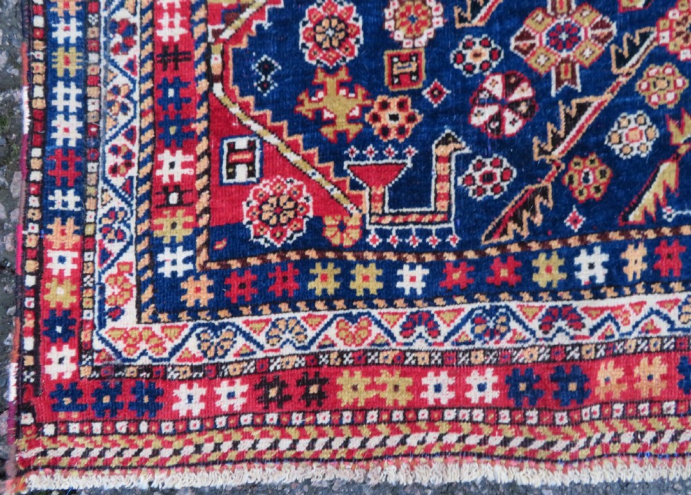 An antique hand-knotted Qashqai wool rug featuring a central ivory diamond medallion surrounded by detailed geometric and animal motifs on a navy blue field with a red border. View IX
