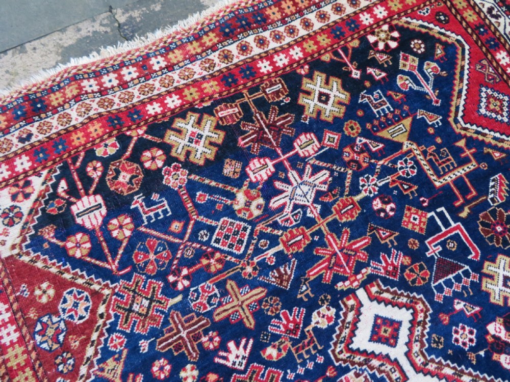 An antique hand-knotted Qashqai wool rug featuring a central ivory diamond medallion surrounded by detailed geometric and animal motifs on a navy blue field with a red border. View XI