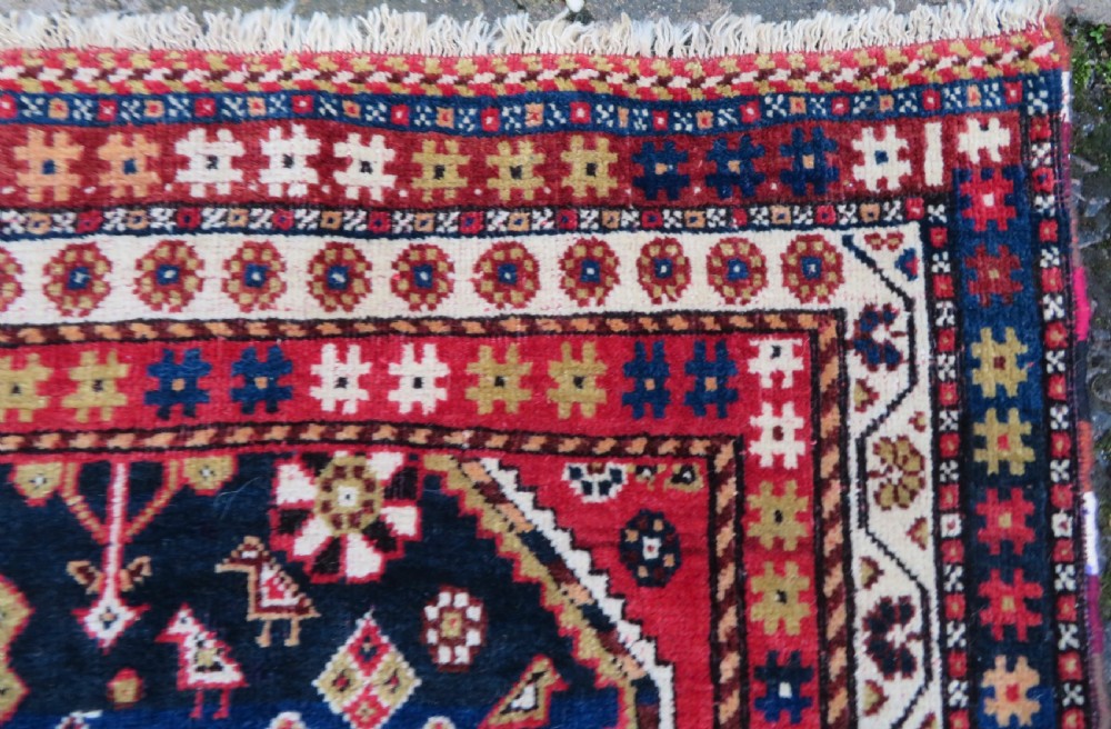 An antique hand-knotted Qashqai wool rug featuring a central ivory diamond medallion surrounded by detailed geometric and animal motifs on a navy blue field with a red border. View XII