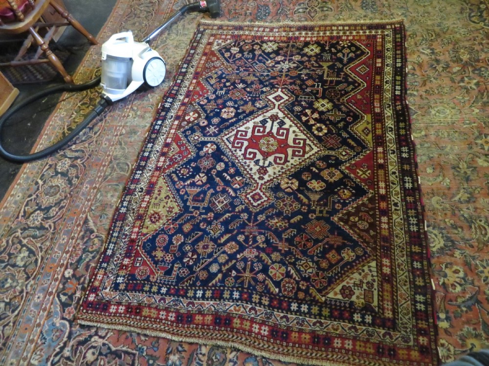 An antique hand-knotted Qashqai wool rug featuring a central ivory diamond medallion surrounded by detailed geometric and animal motifs on a navy blue field with a red border. View XVIII