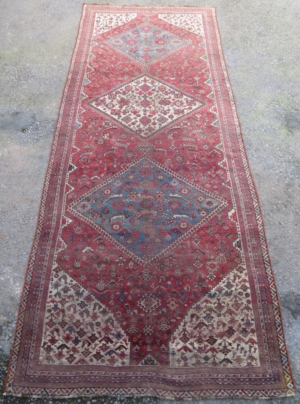 A long hand-knotted antique Persian Khamseh carpet featuring geometric diamond medallions and intricate tribal motifs in red, blue, and cream tones.