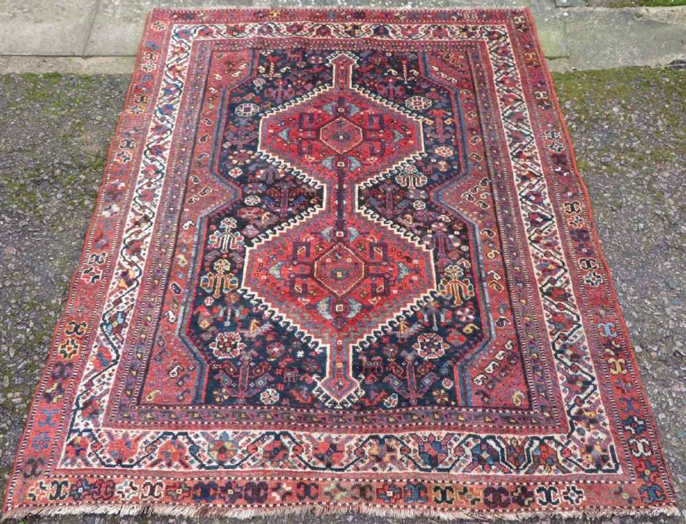An antique Persian Qashqai hand-knotted wool rug with a dark navy blue field, double red geometric medallion, and multi-band patterned borders.