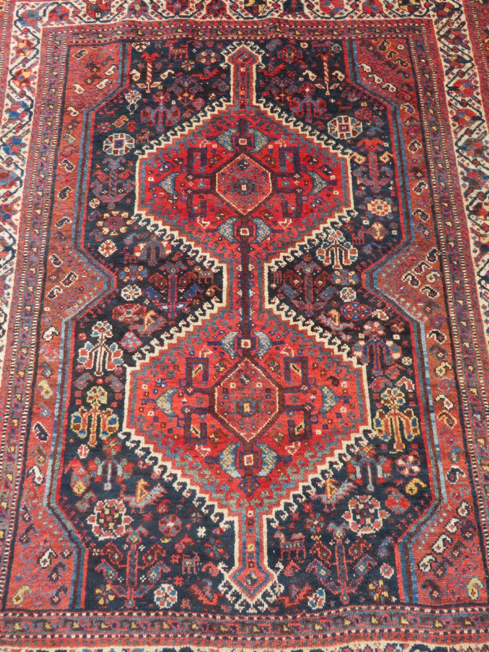 An antique Persian Qashqai hand-knotted wool rug with a dark navy blue field, double red geometric medallion, and multi-band patterned borders. View II