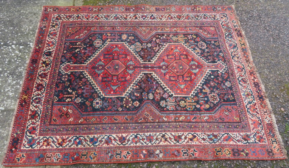 An antique Persian Qashqai hand-knotted wool rug with a dark navy blue field, double red geometric medallion, and multi-band patterned borders. View III