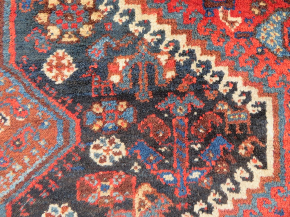 An antique Persian Qashqai hand-knotted wool rug with a dark navy blue field, double red geometric medallion, and multi-band patterned borders. View IV