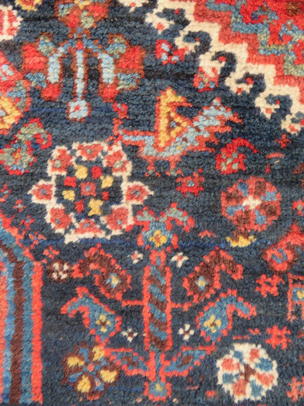 An antique Persian Qashqai hand-knotted wool rug with a dark navy blue field, double red geometric medallion, and multi-band patterned borders. View VI