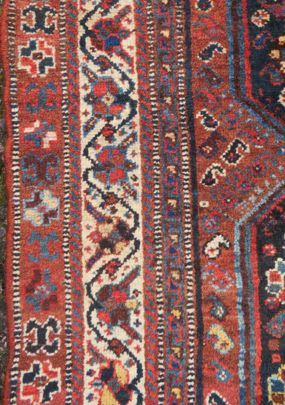 An antique Persian Qashqai hand-knotted wool rug with a dark navy blue field, double red geometric medallion, and multi-band patterned borders. View IX
