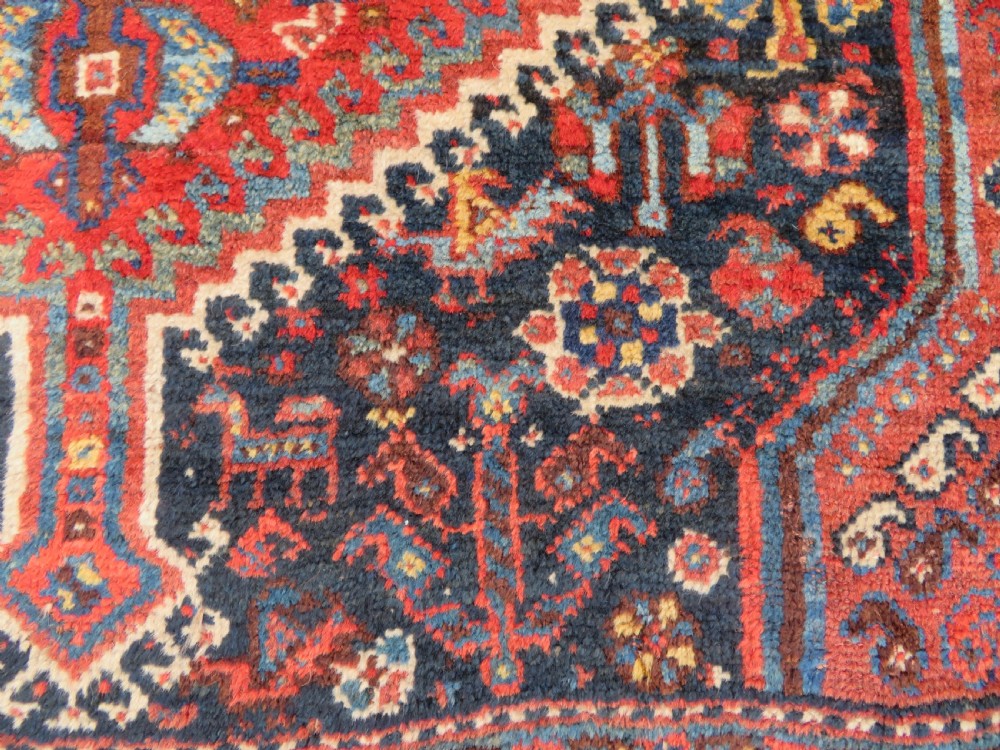 An antique Persian Qashqai hand-knotted wool rug with a dark navy blue field, double red geometric medallion, and multi-band patterned borders. View X