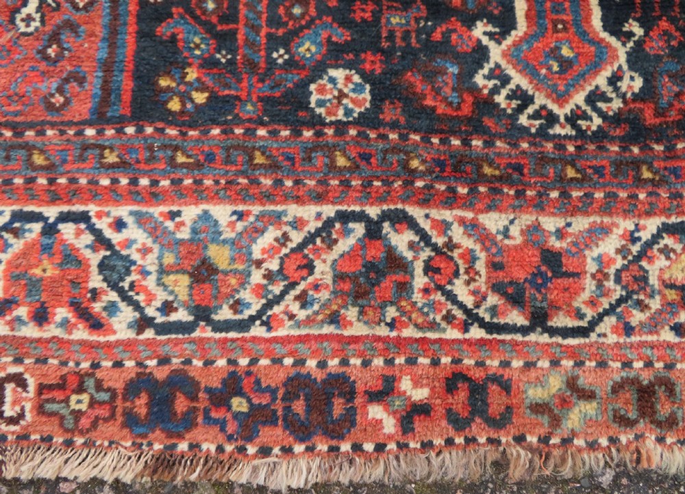 An antique Persian Qashqai hand-knotted wool rug with a dark navy blue field, double red geometric medallion, and multi-band patterned borders. View XI