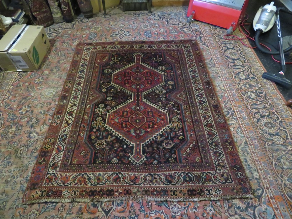 An antique Persian Qashqai hand-knotted wool rug with a dark navy blue field, double red geometric medallion, and multi-band patterned borders. View XVIII