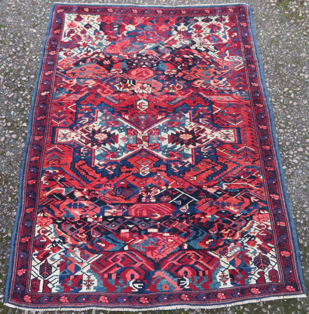 A rectangular hand-knotted antique Caucasian Kuba rug featuring complex geometric motifs in deep red, navy blue, light blue, and cream. View II