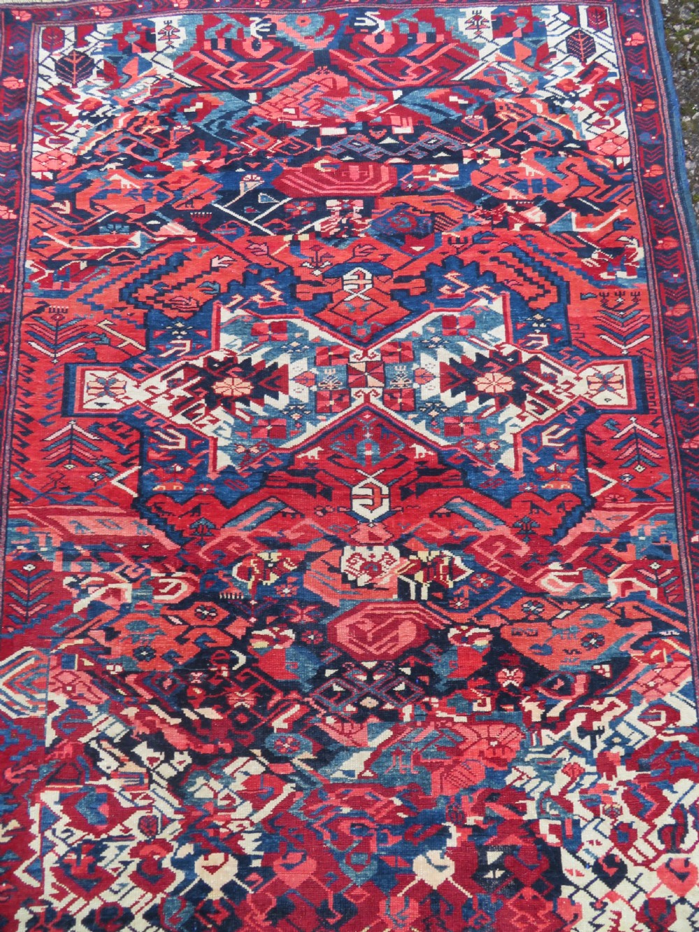 A rectangular hand-knotted antique Caucasian Kuba rug featuring complex geometric motifs in deep red, navy blue, light blue, and cream. View III