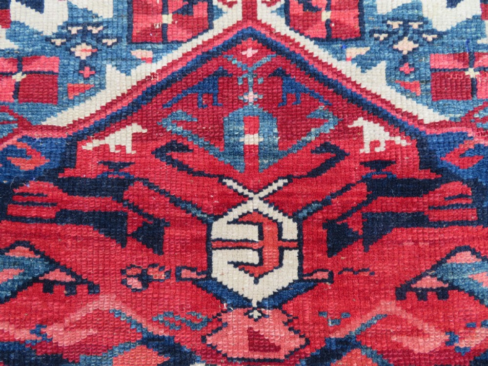 A rectangular hand-knotted antique Caucasian Kuba rug featuring complex geometric motifs in deep red, navy blue, light blue, and cream. View IV
