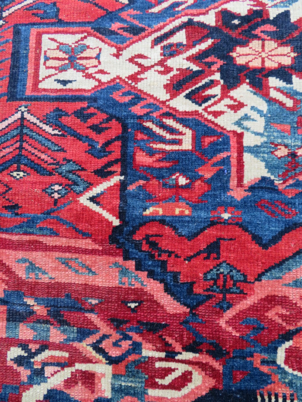 A rectangular hand-knotted antique Caucasian Kuba rug featuring complex geometric motifs in deep red, navy blue, light blue, and cream. View V