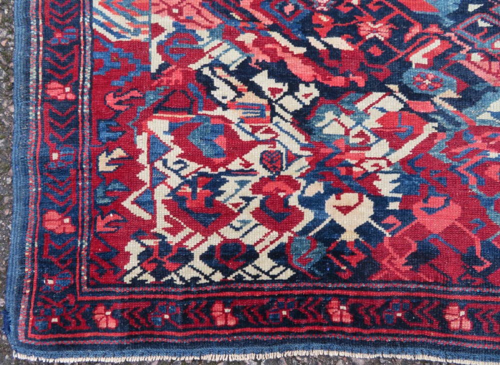 A rectangular hand-knotted antique Caucasian Kuba rug featuring complex geometric motifs in deep red, navy blue, light blue, and cream. View IX