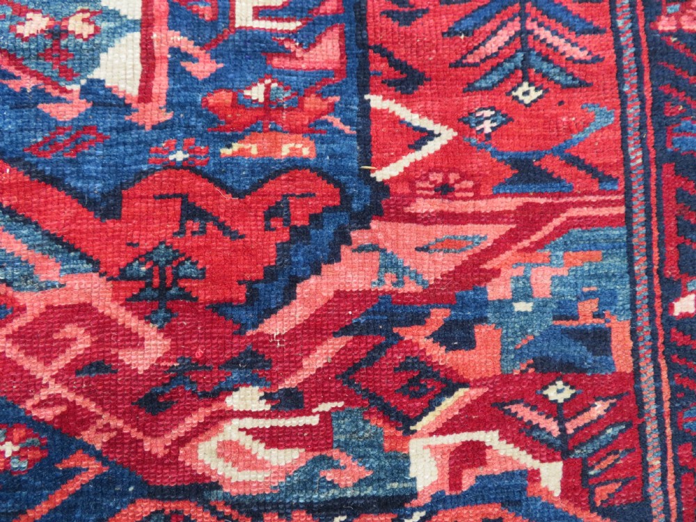 A rectangular hand-knotted antique Caucasian Kuba rug featuring complex geometric motifs in deep red, navy blue, light blue, and cream. View XV