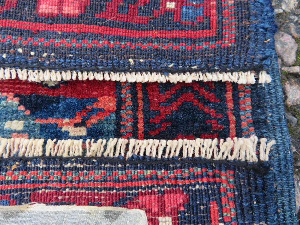A rectangular hand-knotted antique Caucasian Kuba rug featuring complex geometric motifs in deep red, navy blue, light blue, and cream. View XIX