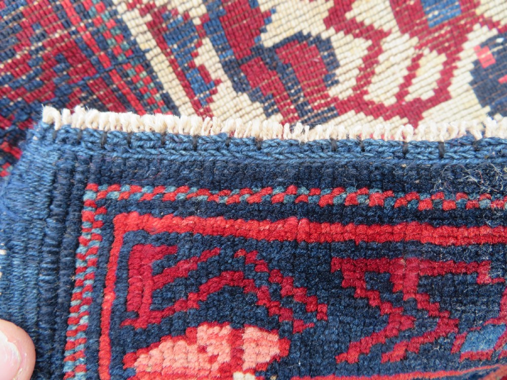 A rectangular hand-knotted antique Caucasian Kuba rug featuring complex geometric motifs in deep red, navy blue, light blue, and cream. View XX