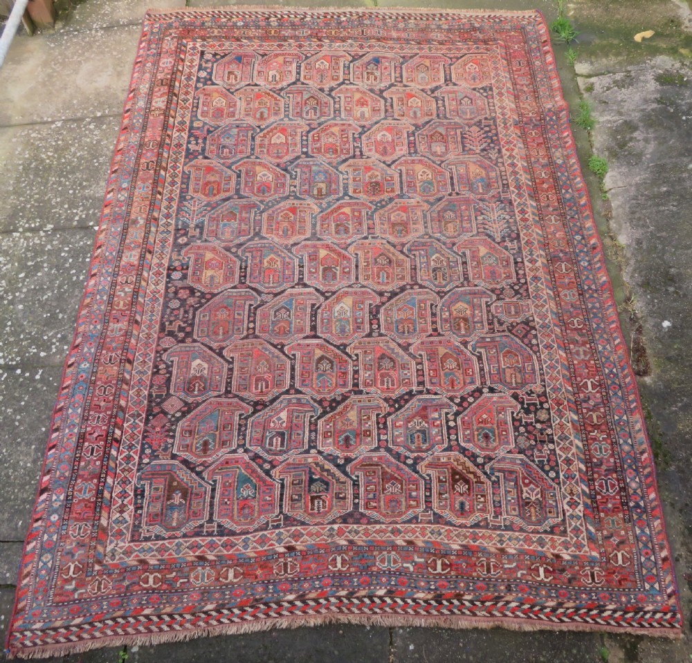 An antique Khamseh hand-knotted wool carpet featuring repeating stylised boteh motifs on a dark navy field with multi-banded geometric borders.