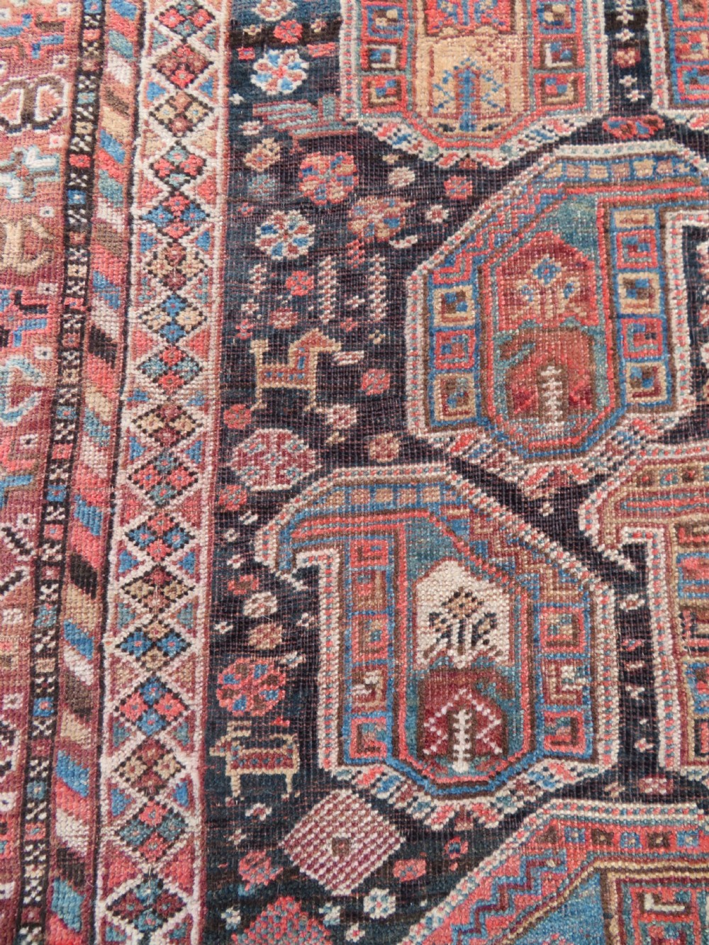 An antique Khamseh hand-knotted wool carpet featuring repeating stylised boteh motifs on a dark navy field with multi-banded geometric borders. View V