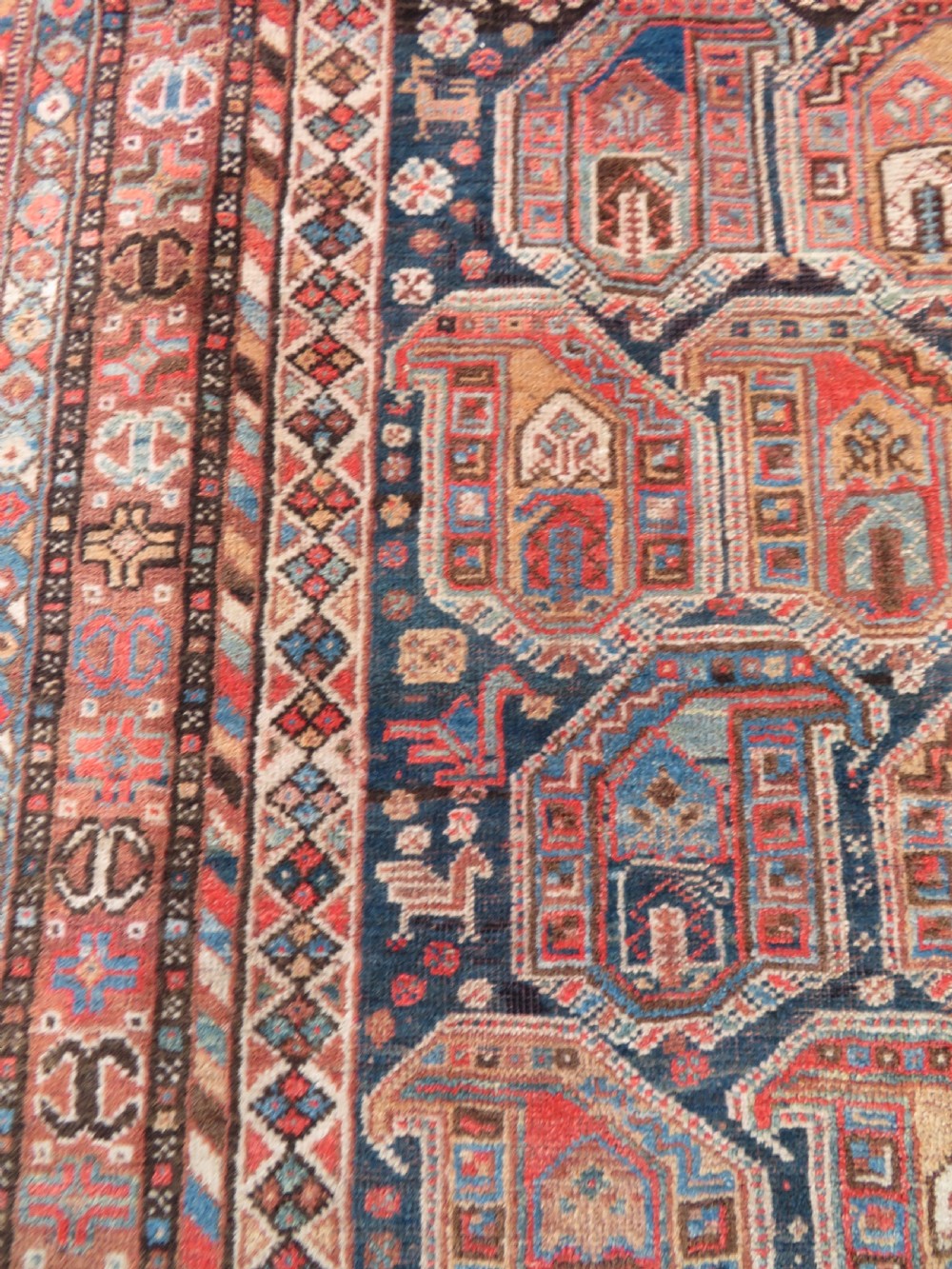 An antique Khamseh hand-knotted wool carpet featuring repeating stylised boteh motifs on a dark navy field with multi-banded geometric borders. View VII