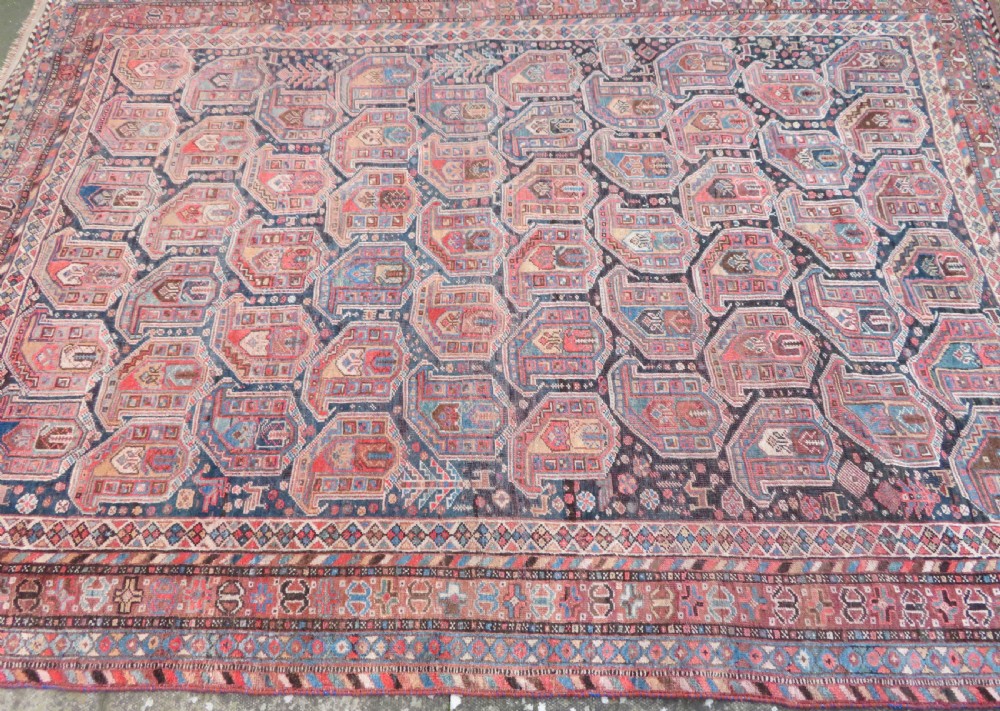An antique Khamseh hand-knotted wool carpet featuring repeating stylised boteh motifs on a dark navy field with multi-banded geometric borders. View XX