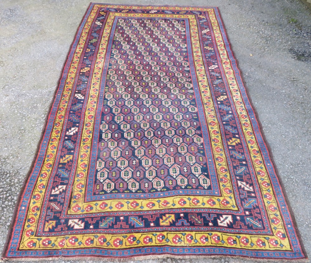 An antique hand-knotted Kurdish Kelleh long rug featuring a navy blue central field filled with repeating geometric motifs within multi-coloured yellow and red borders.