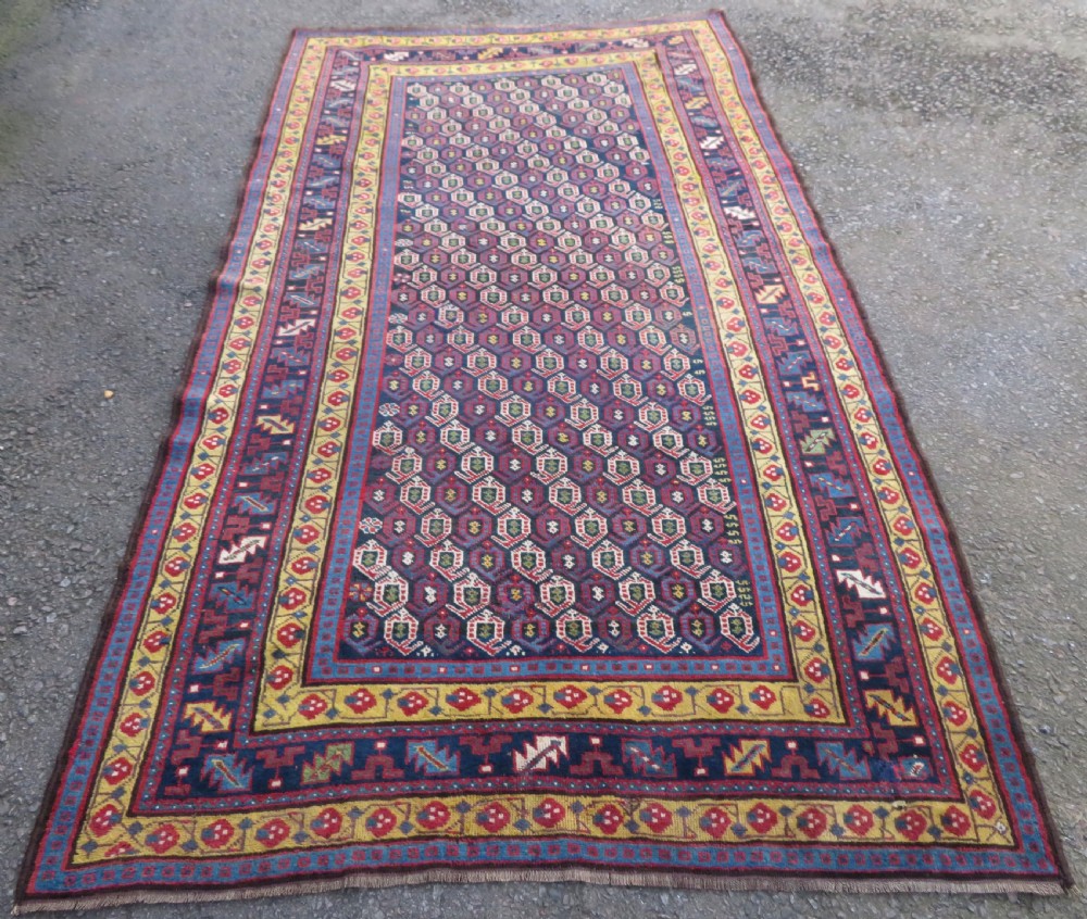 An antique hand-knotted Kurdish Kelleh long rug featuring a navy blue central field filled with repeating geometric motifs within multi-coloured yellow and red borders. View II
