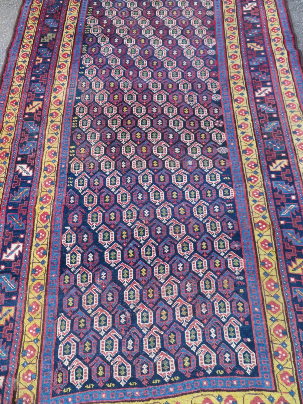 An antique hand-knotted Kurdish Kelleh long rug featuring a navy blue central field filled with repeating geometric motifs within multi-coloured yellow and red borders. View III