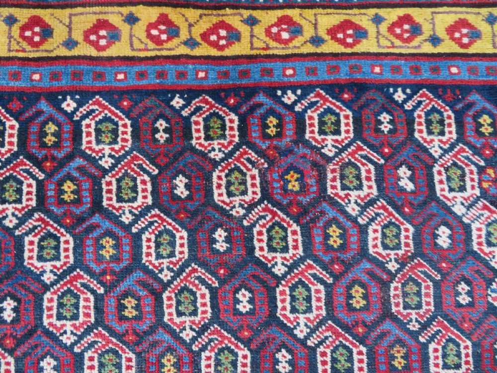 An antique hand-knotted Kurdish Kelleh long rug featuring a navy blue central field filled with repeating geometric motifs within multi-coloured yellow and red borders. View IV