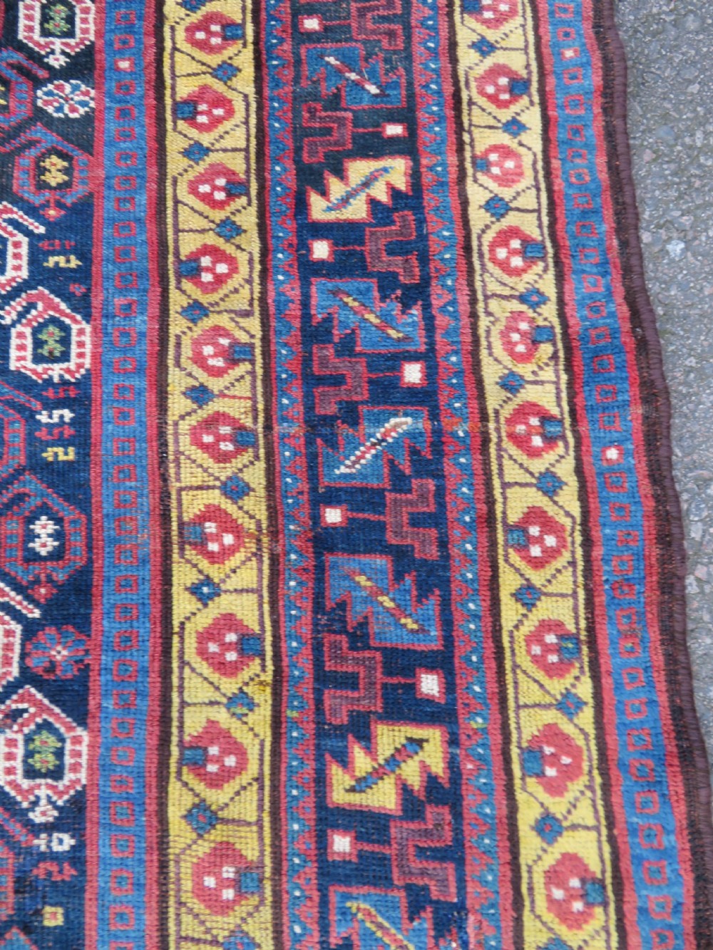 An antique hand-knotted Kurdish Kelleh long rug featuring a navy blue central field filled with repeating geometric motifs within multi-coloured yellow and red borders. View V